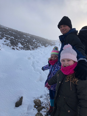 a father walking along a snowy trial with his two daughters who are all looking back for a picture