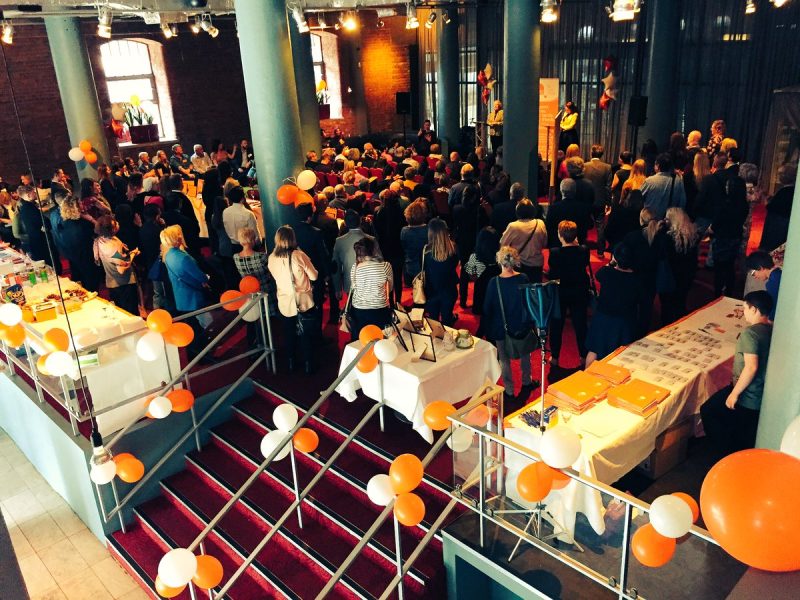 a room full of people from behind with orange balloons and white balloons