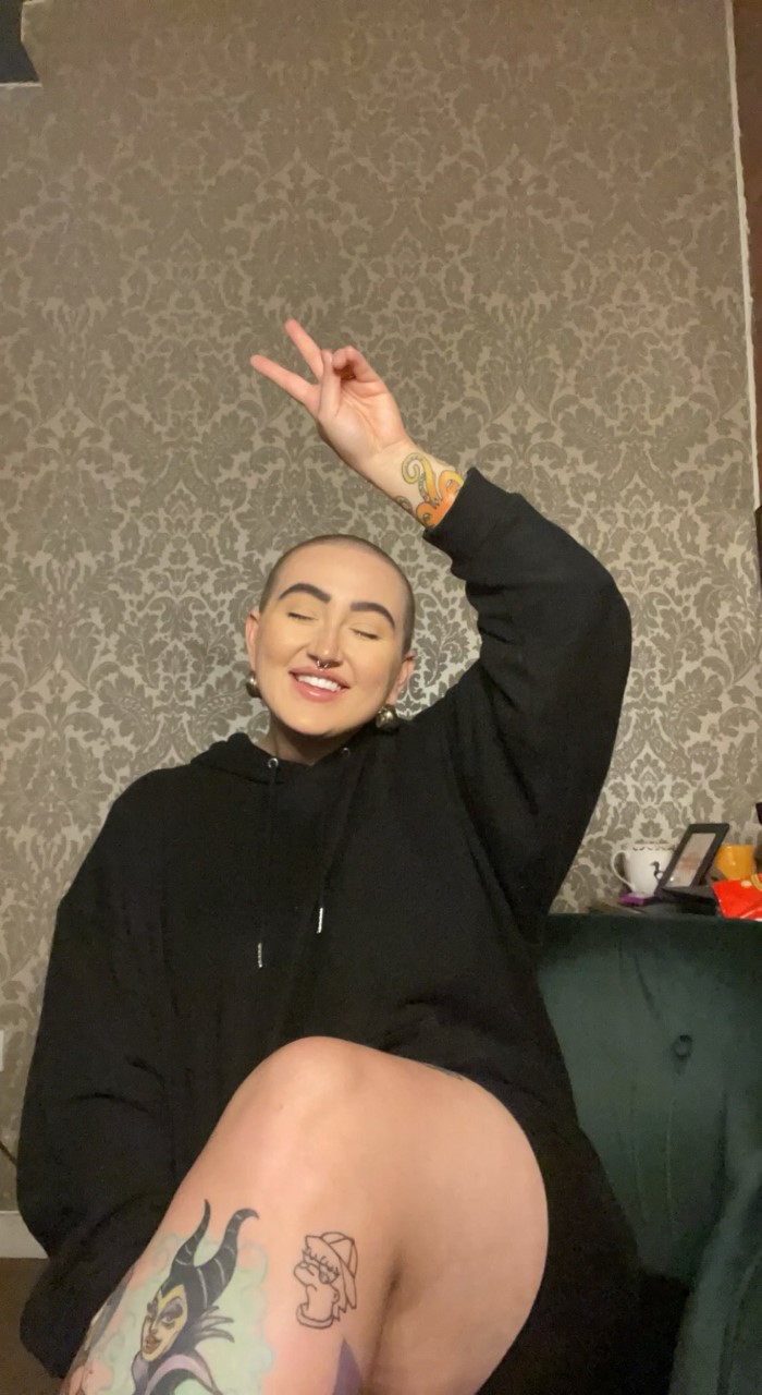 a woman with tattoo on her leg posing and smiling with a shaved head