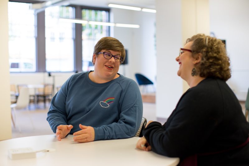 two woman sat a table chatting a smiling