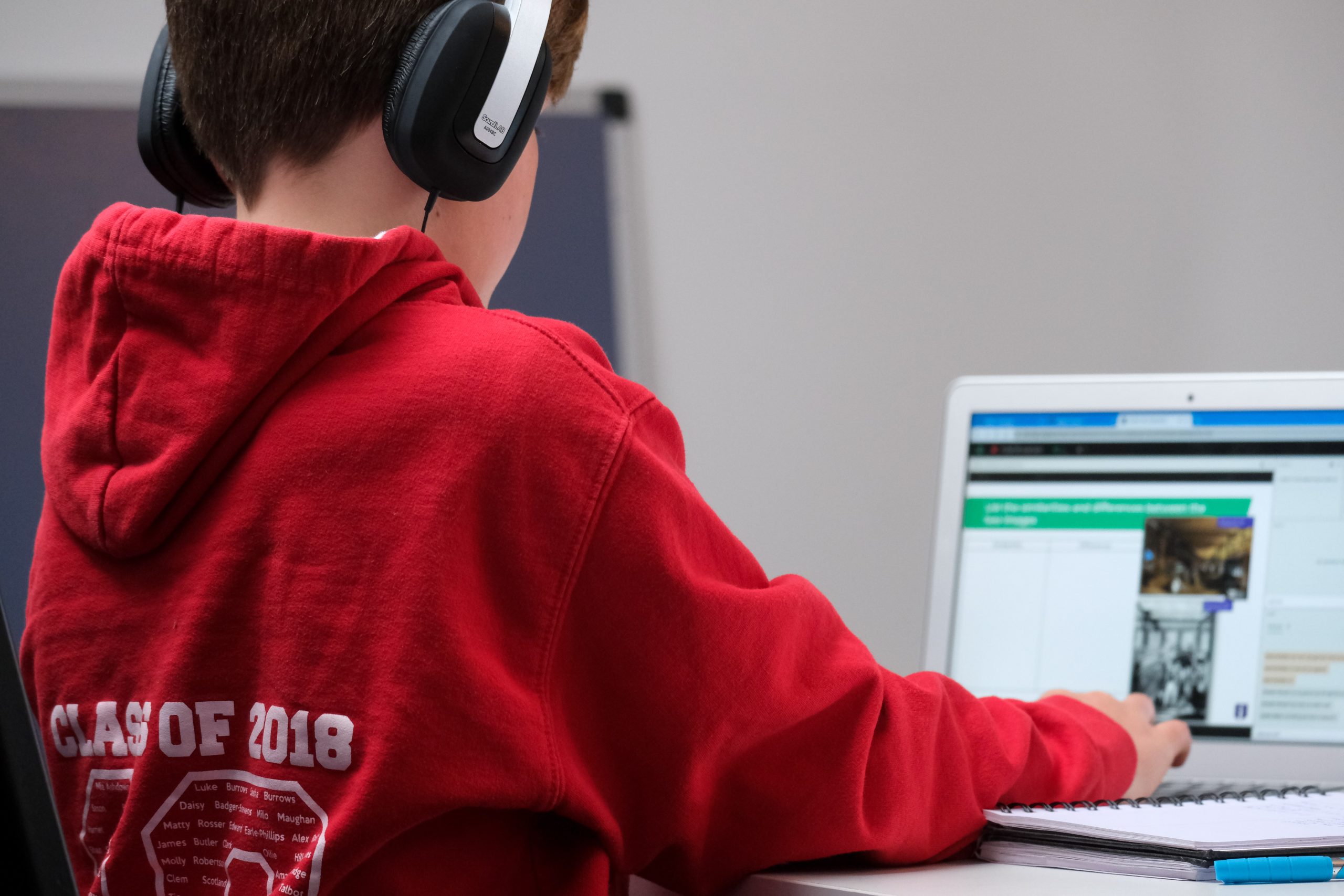 a young boy with head phones on sat at a desk on a laptop watching something