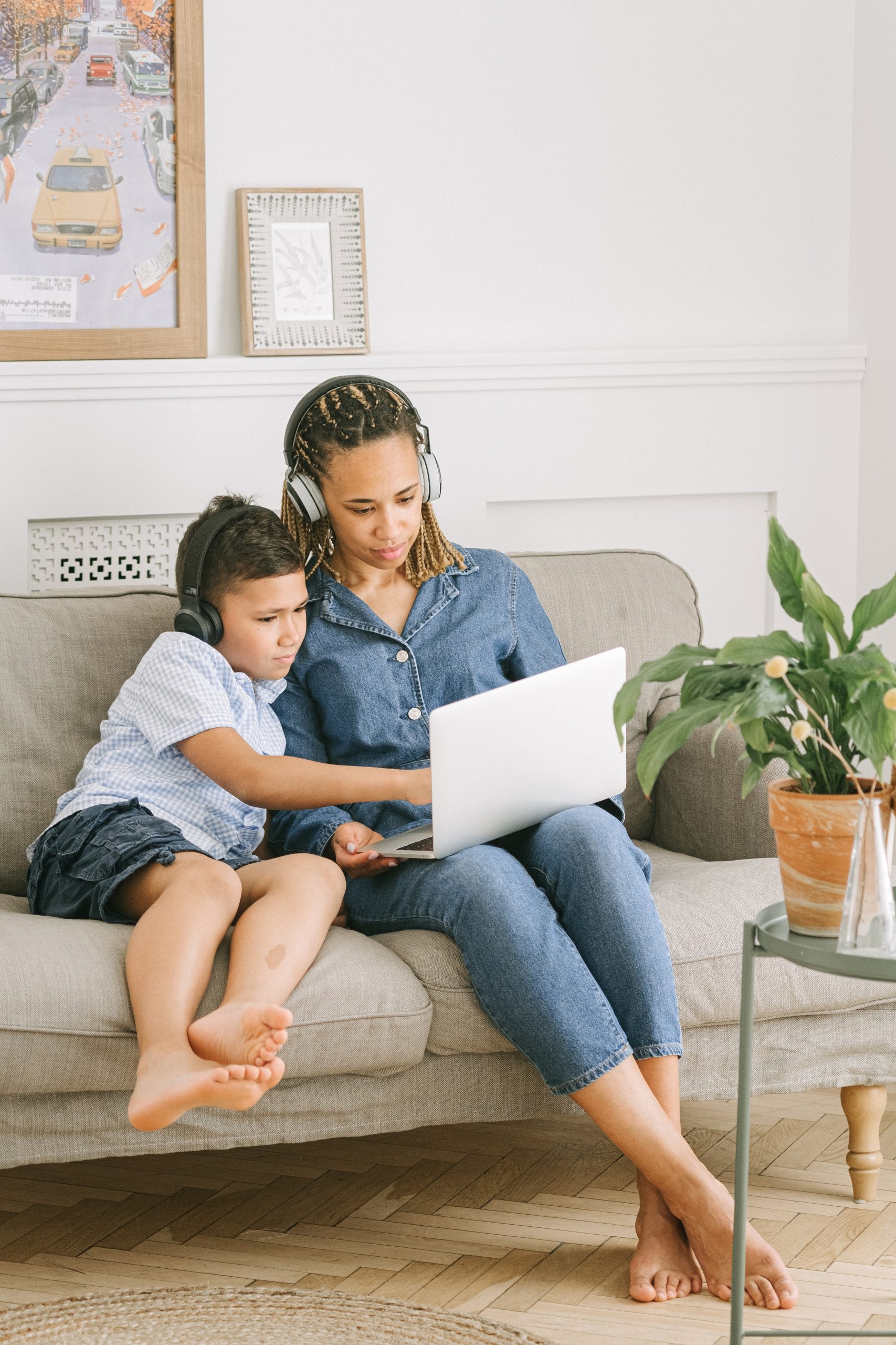 a mother and her son sat on a couch with headphones on watching something on a laptop