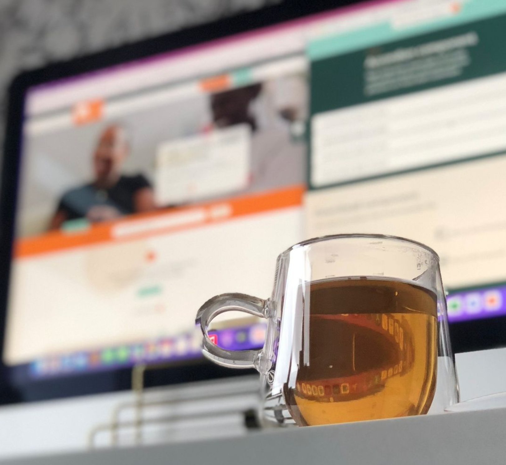 a picture of a clear mug with tea in and a website on a laptop in the behind blurred