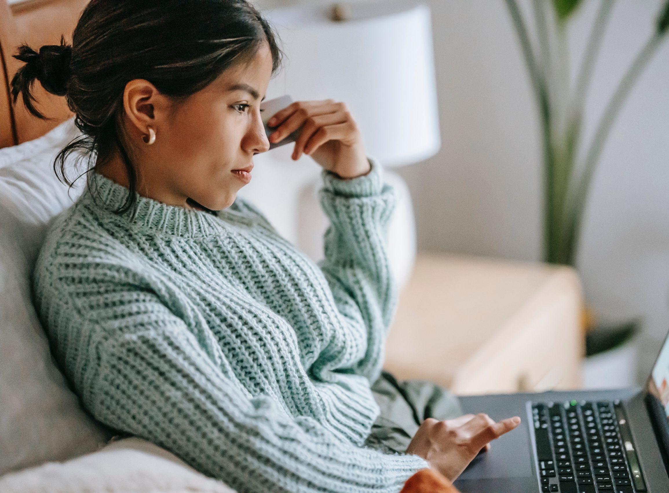 a woman wearing a grey knit jumper sat scowling on a a computer from the side