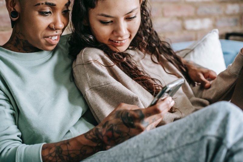 two women sat down both smiling looking at something on a phone