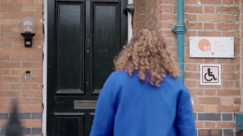 a woman with curly hair from behind walking up to a black door
