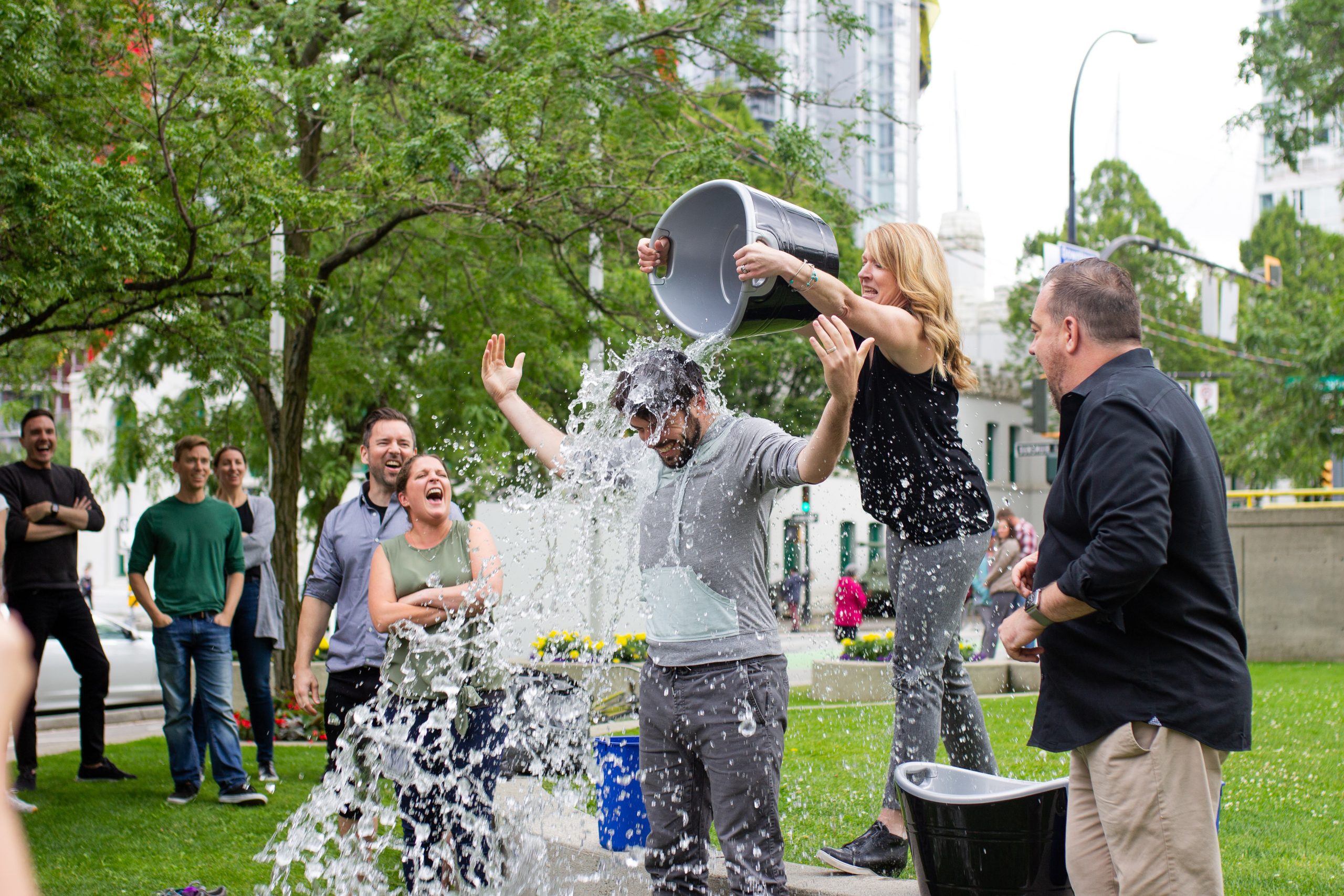 a woman dumping a bucket of water over a man with people surrounding laughing