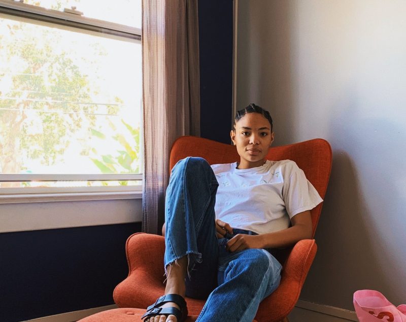 a woman sat on an orange arm chair looking directly at the camera