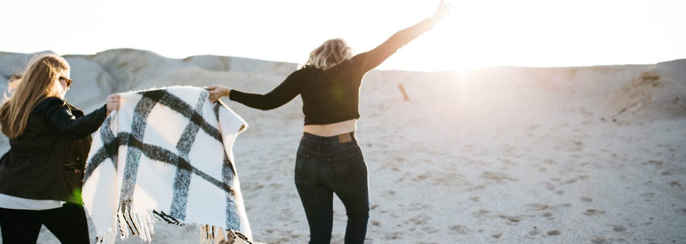 two women on a beach holding a blanket as they step over something