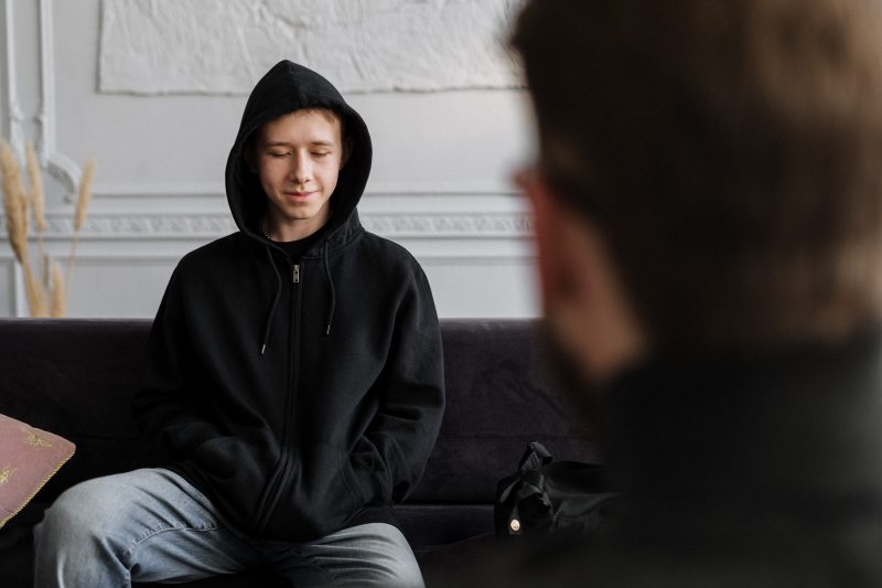 a young man sat with a hooded jacket talking to someone out of the picture