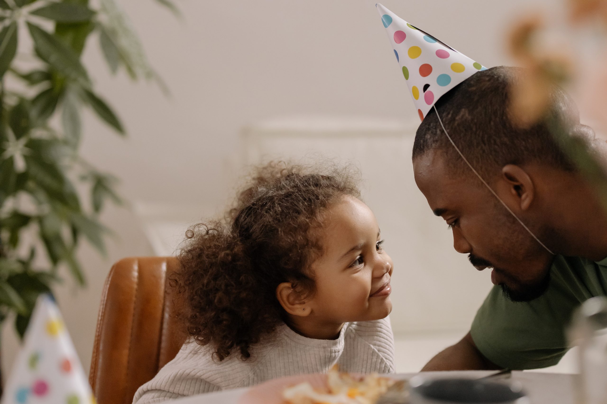 man with a birthday hat hat talking to his young daughter who is smiling