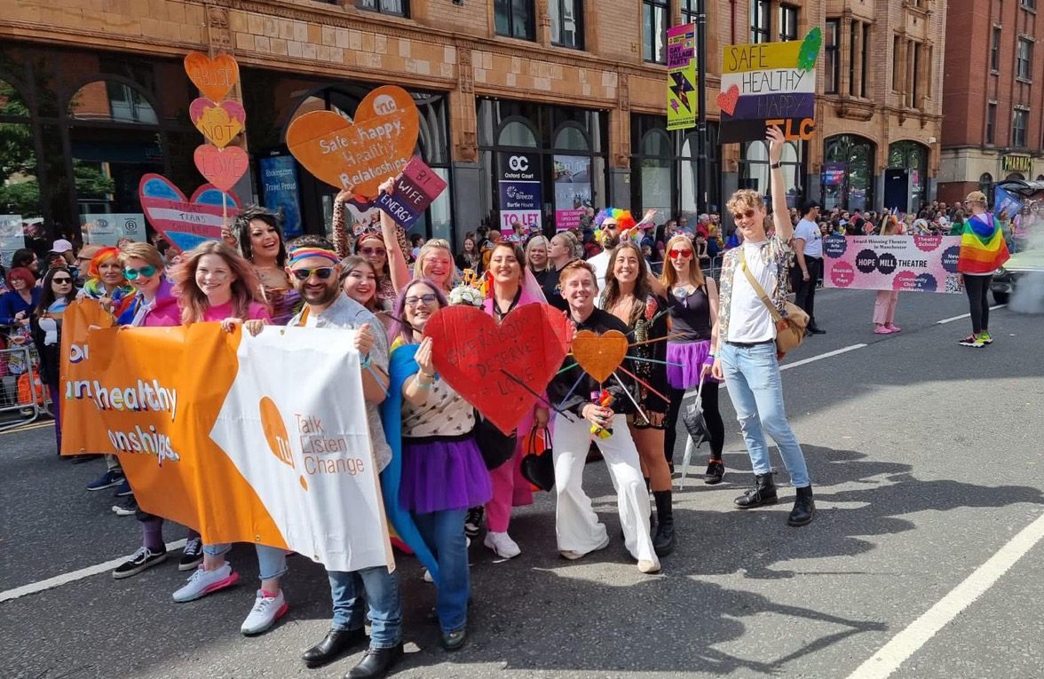 a group of people in the Manchester pride parade holding a TLC: Talk, Listen, Change banner