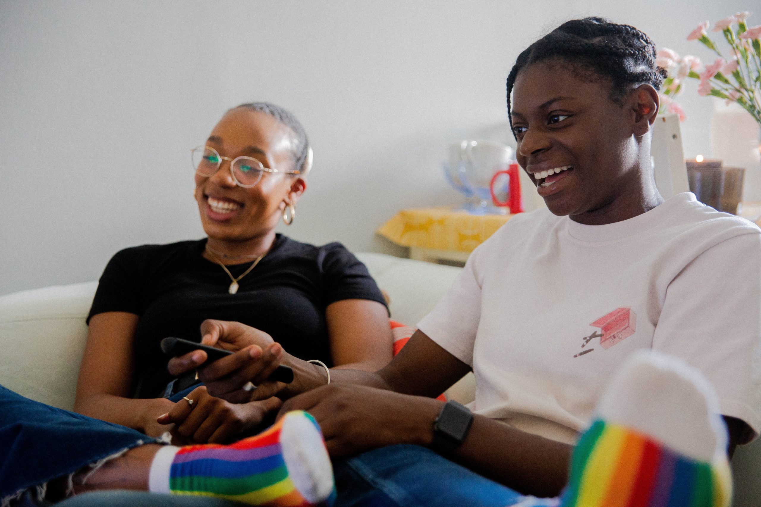 two people sat on a couch smiling whilst one has a remote in their hand looking at something out of picture