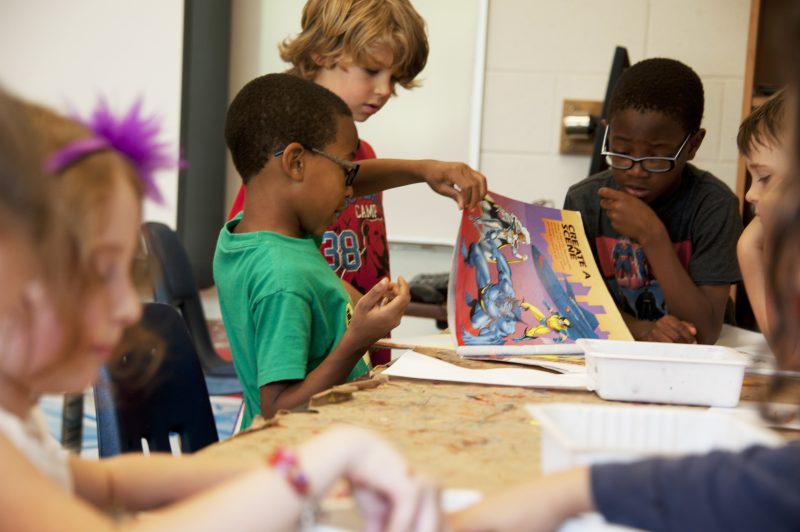 a group of young children sat at a table with colouring supplies