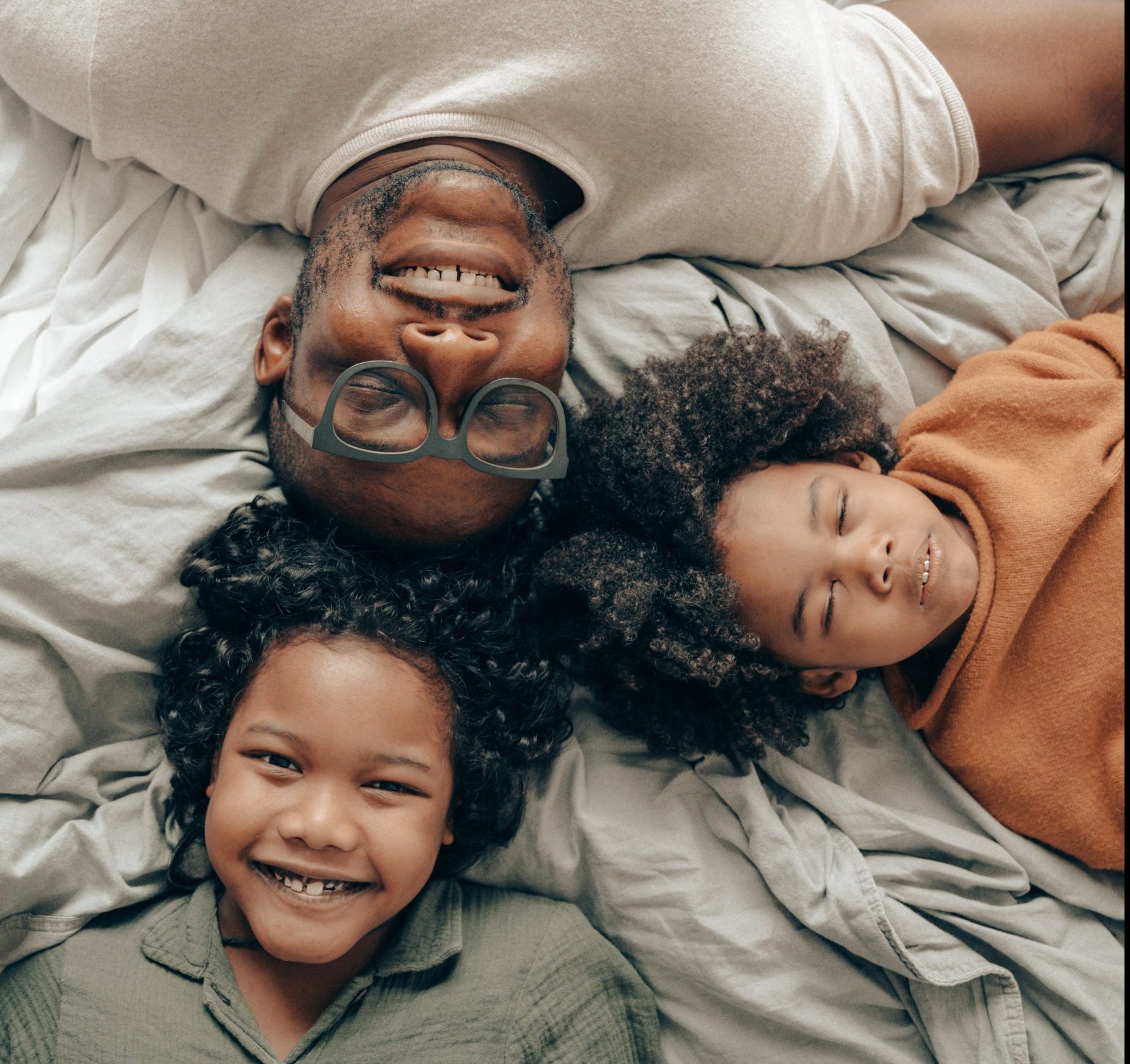 Man with glasses with his two curls dark haired sons all touching heads laying down.