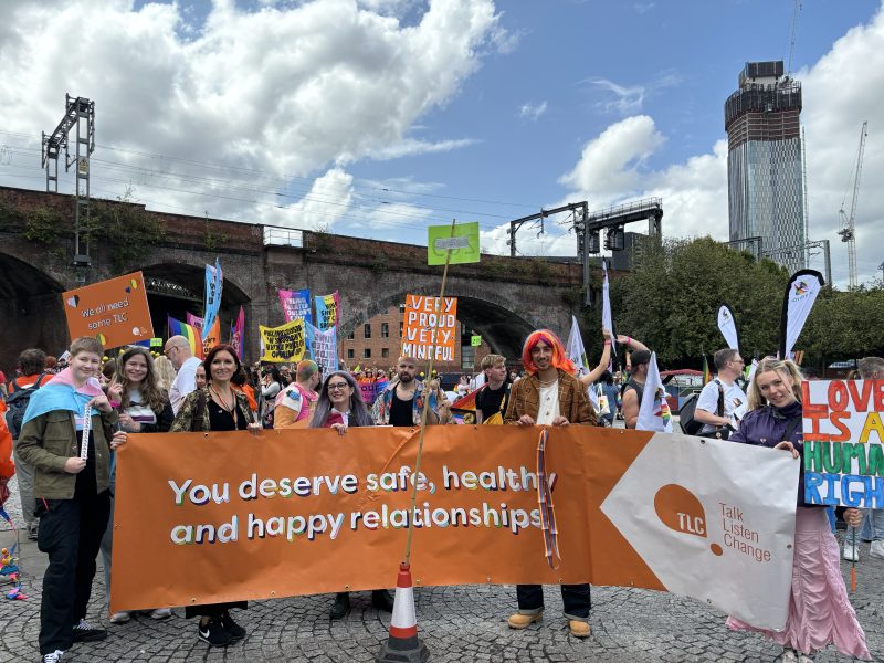 a group of people holding and posing with a TLC: Talk, Listen, Change long banner