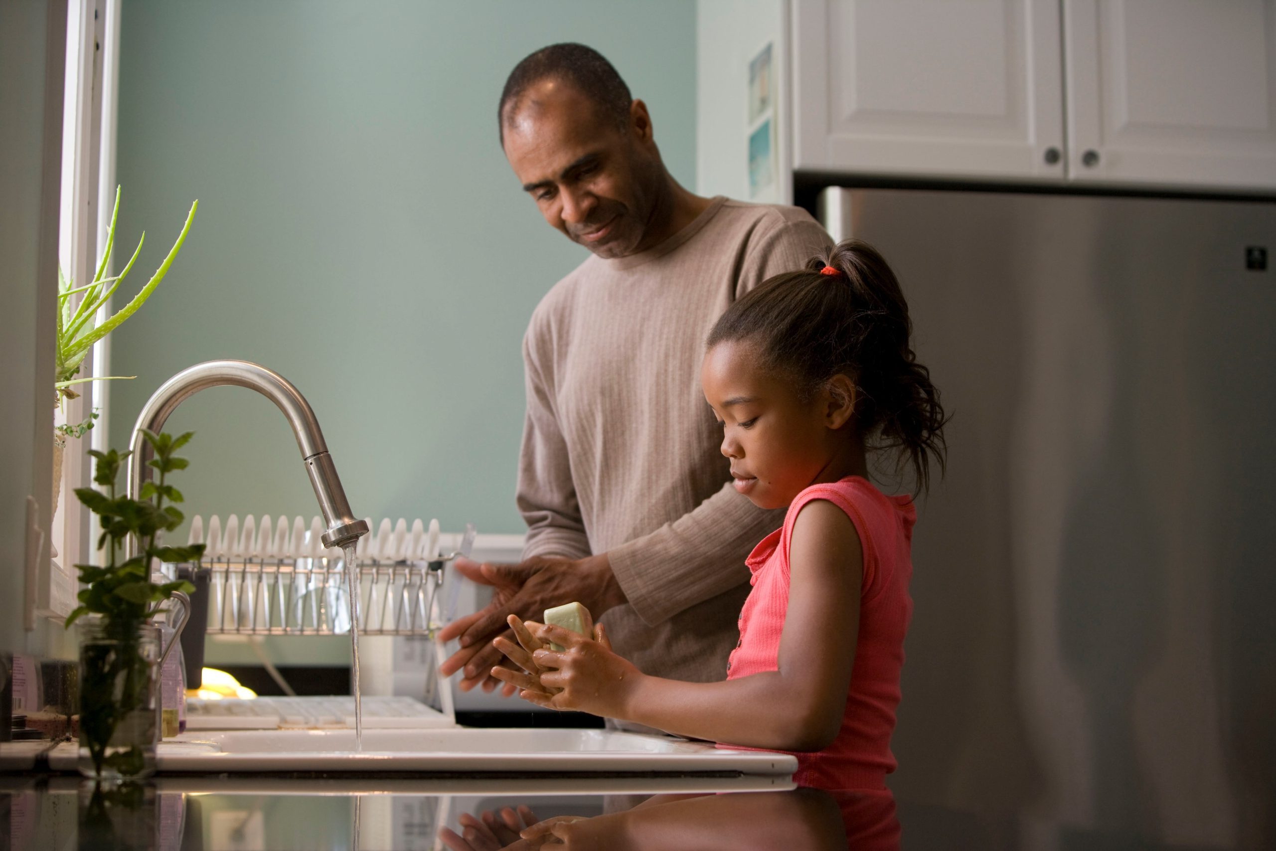 Man and his daughter washing their hand in a kitchen sink