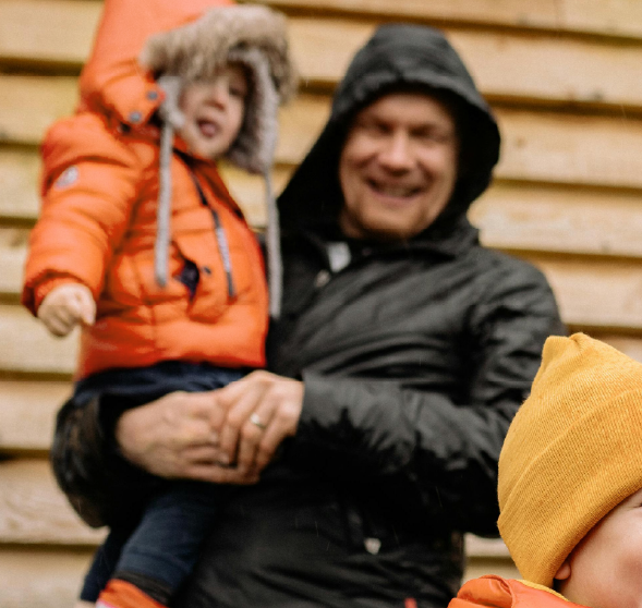 a man holding a child with an orange quote in the blurred background with another child a the centre with an orange quote