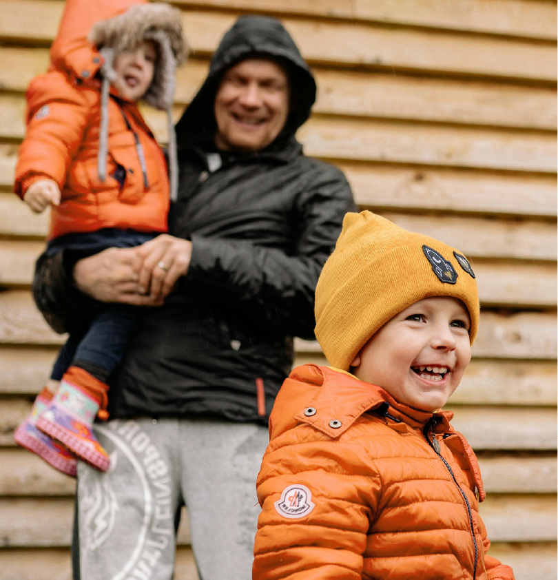 a man holding a child with an orange quote in the blurred background with another child a the centre with an orange quote