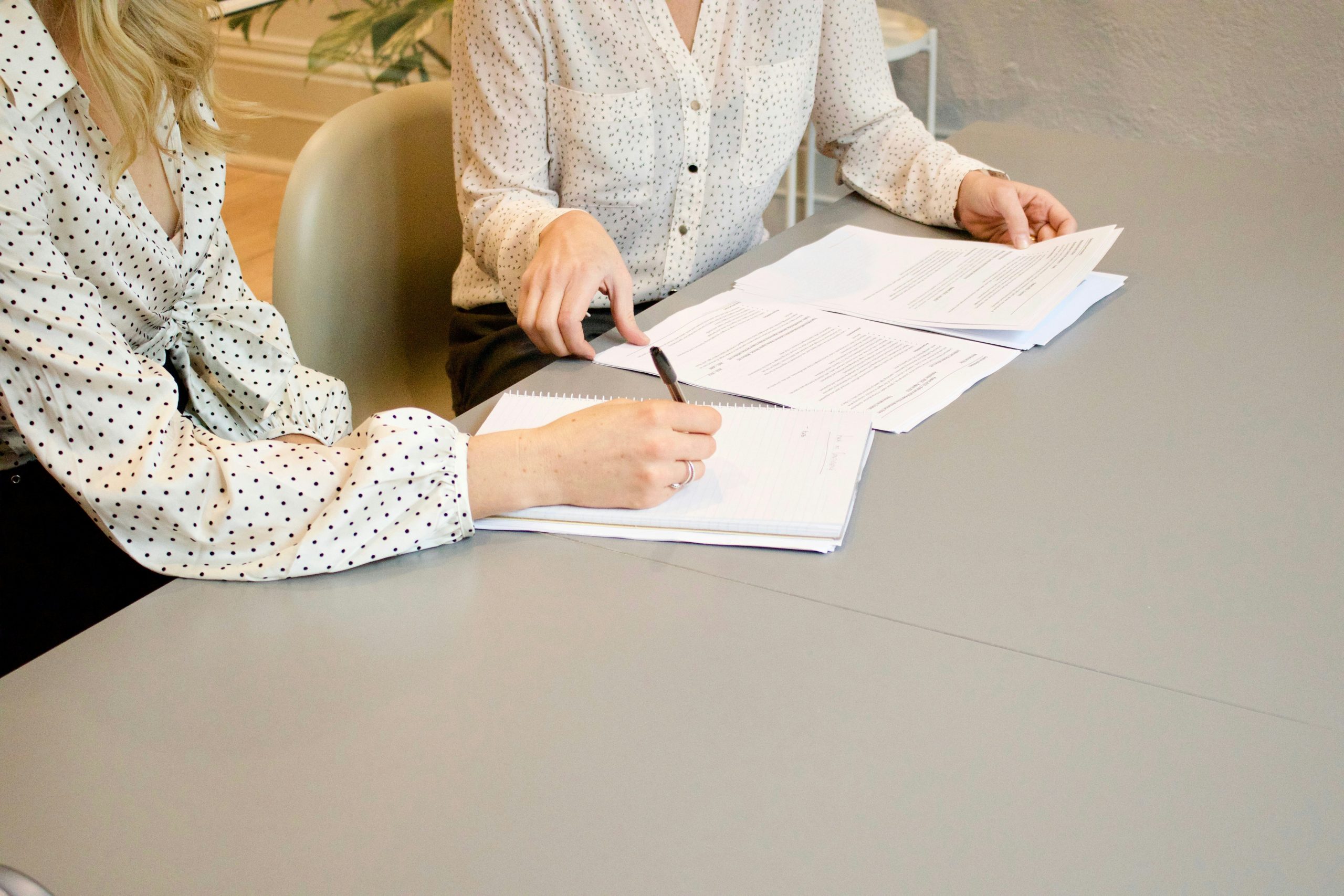 Two women sat at a table signing with documents in front of them making notes