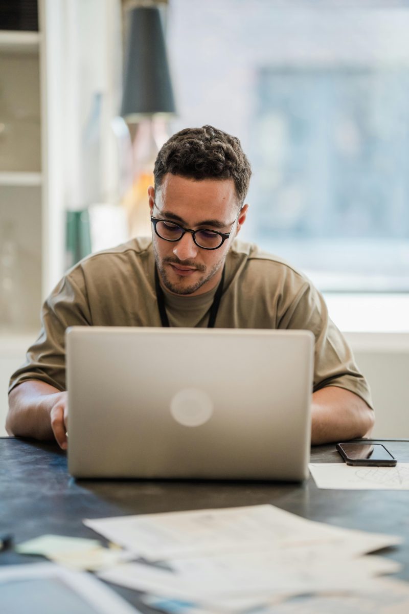 a man sat at a desk with a laptop open researching something