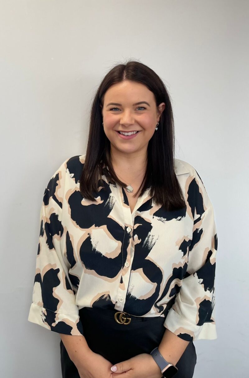 A woman with dark hair and a print blouse stood in front of a white background