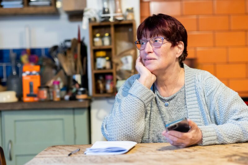 Woman with short red hair sat in a cafe with her phone in her hand and paperwork on the table
