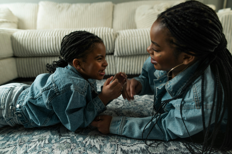 black mother and daughter on a lounge floor, chatting and smiling.