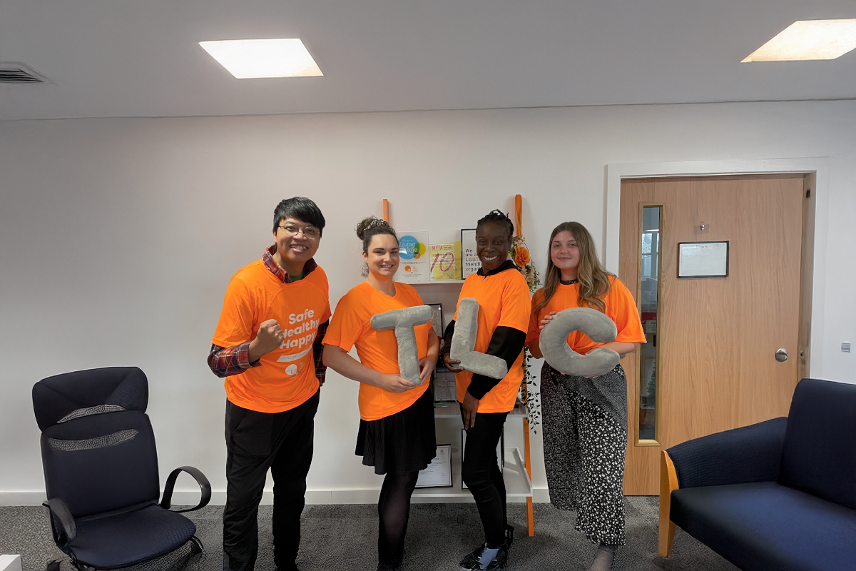 team members in matching orange sports tops posing in a workplace office.