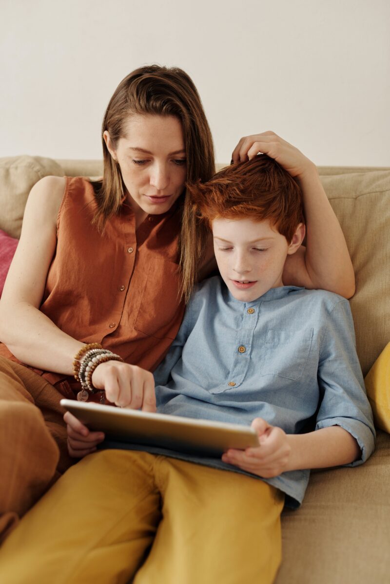 Mother and son sat on a sofa sharing the use of an iPad.