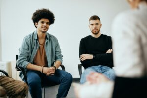 two man can be seen sat within a group setting, sat in a circle.