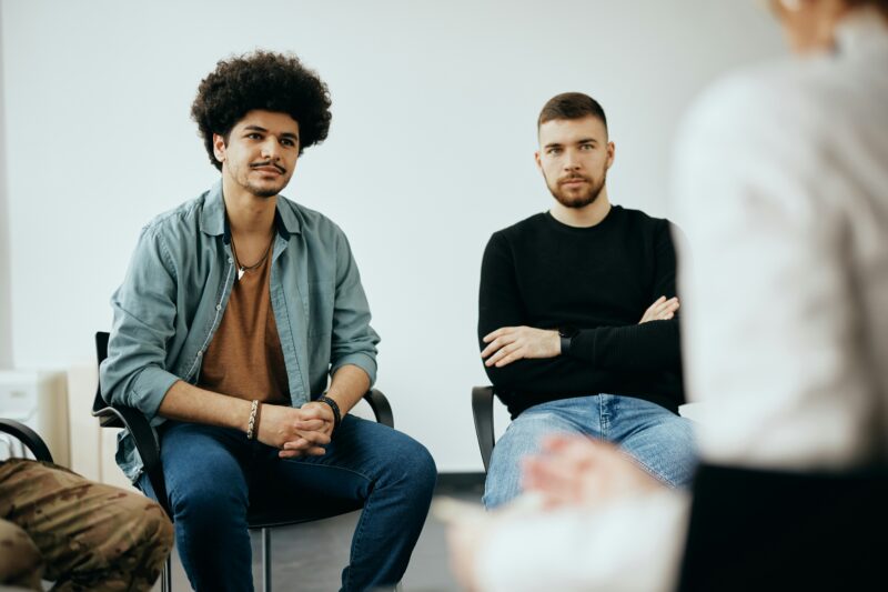 two man can be seen sat within a group setting, sat in a circle.
