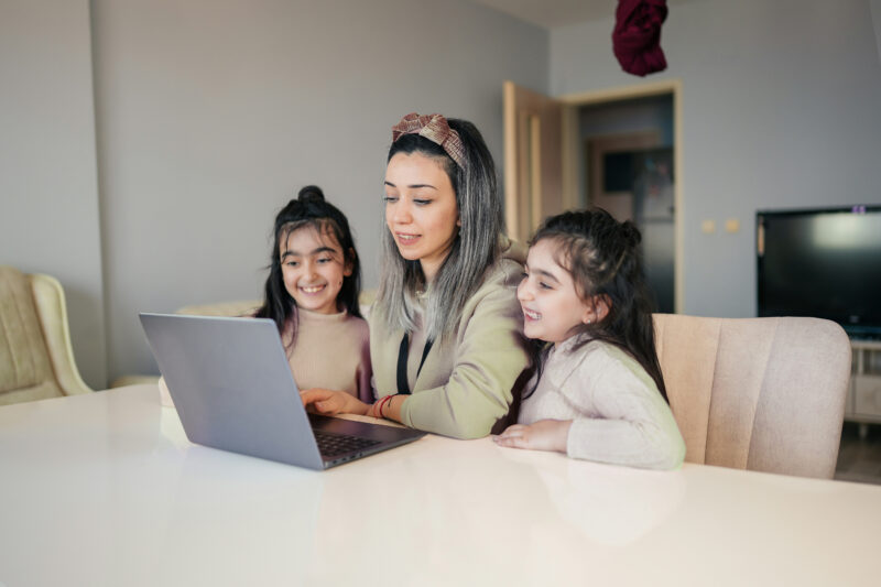A mother siting a table with her laptop in front of her with two children sat either side of her