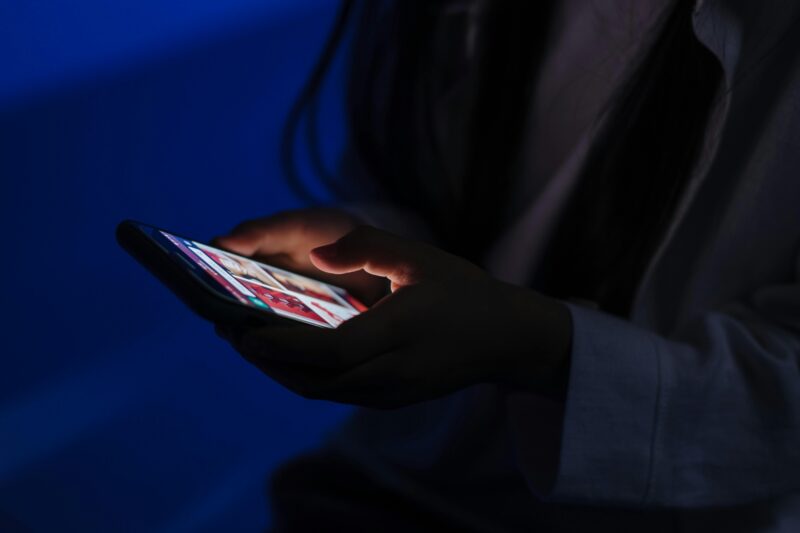 Young girl in a dark blue light room looking at something on her phone