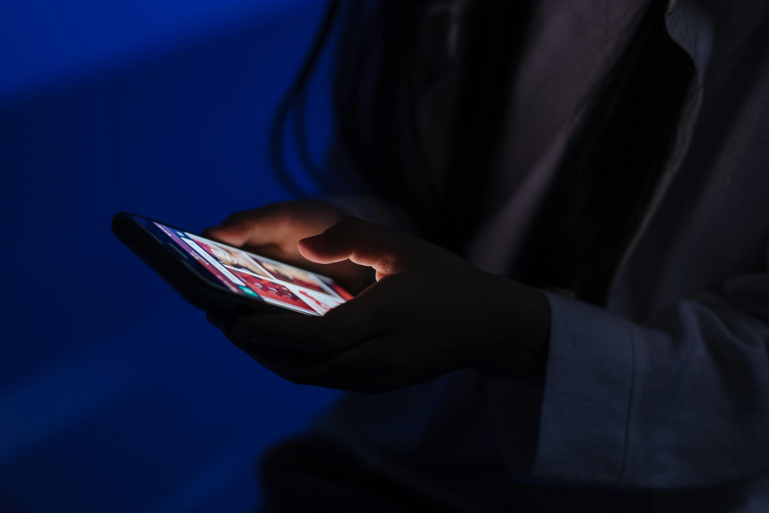 Young girl in a dark blue light room looking at something on her phone