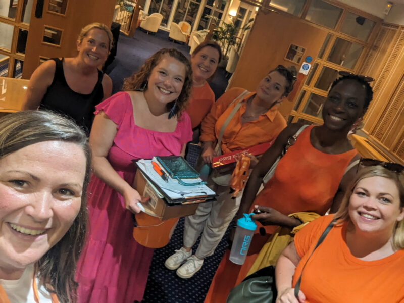 selfie of a group of women who are all dressed in orange and holding charity fundraising buckets