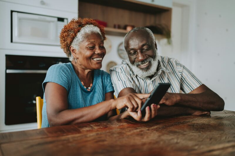 older black couple sit at the dining room table, looking connected to one another.