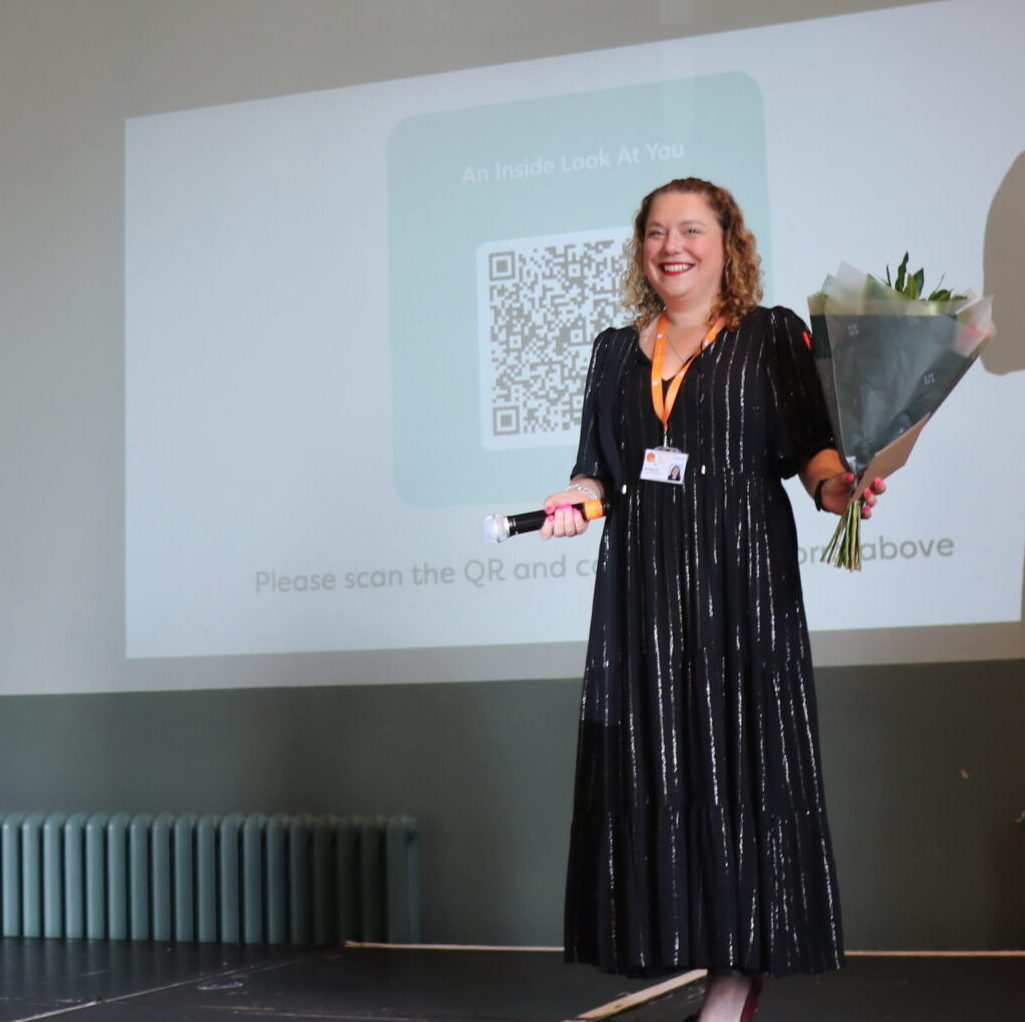 TLC CEO hands flowers to longest-served TLC employee on a stage infront of a screen projection.